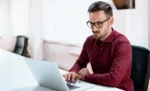 Dividendos em empresas sem lucro contábil: é possível? Homem trabalhando em seu notebook sobre uma mesa em ambiente de escritório representando: Dividendos em empresas sem lucro contábil: é possível?